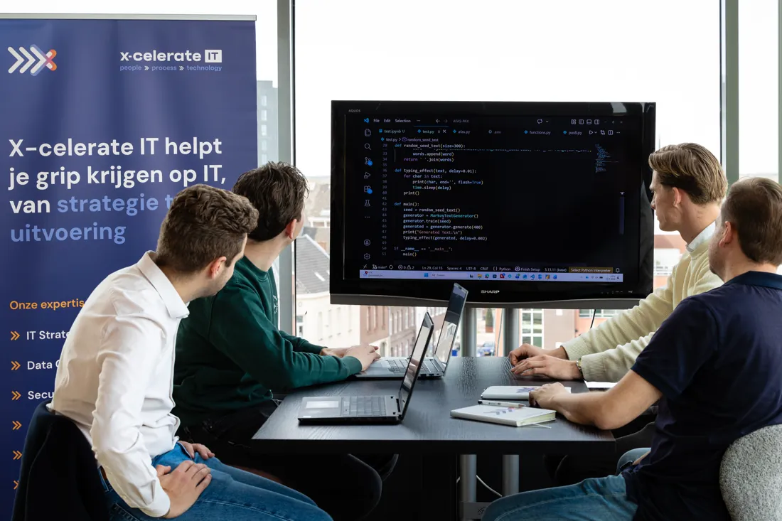 Het X-celerate team kijkt samen aan tafel naar het scherm